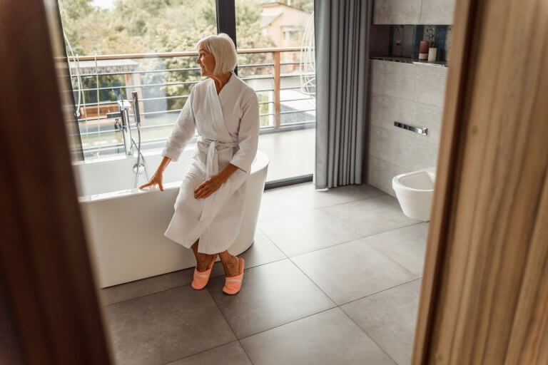 Joyful senior lady in bathrobe looking out of the window